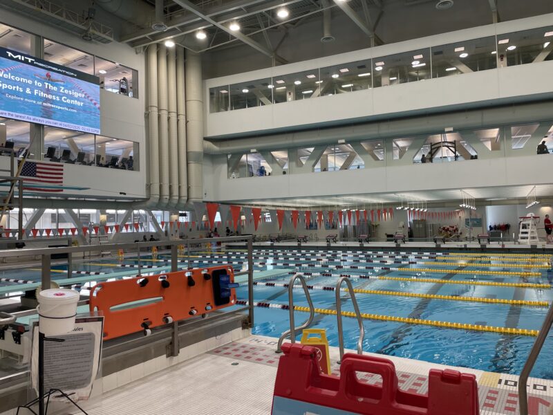 MIT's swimming pool with colorful flags above the water and a gym above the pool.