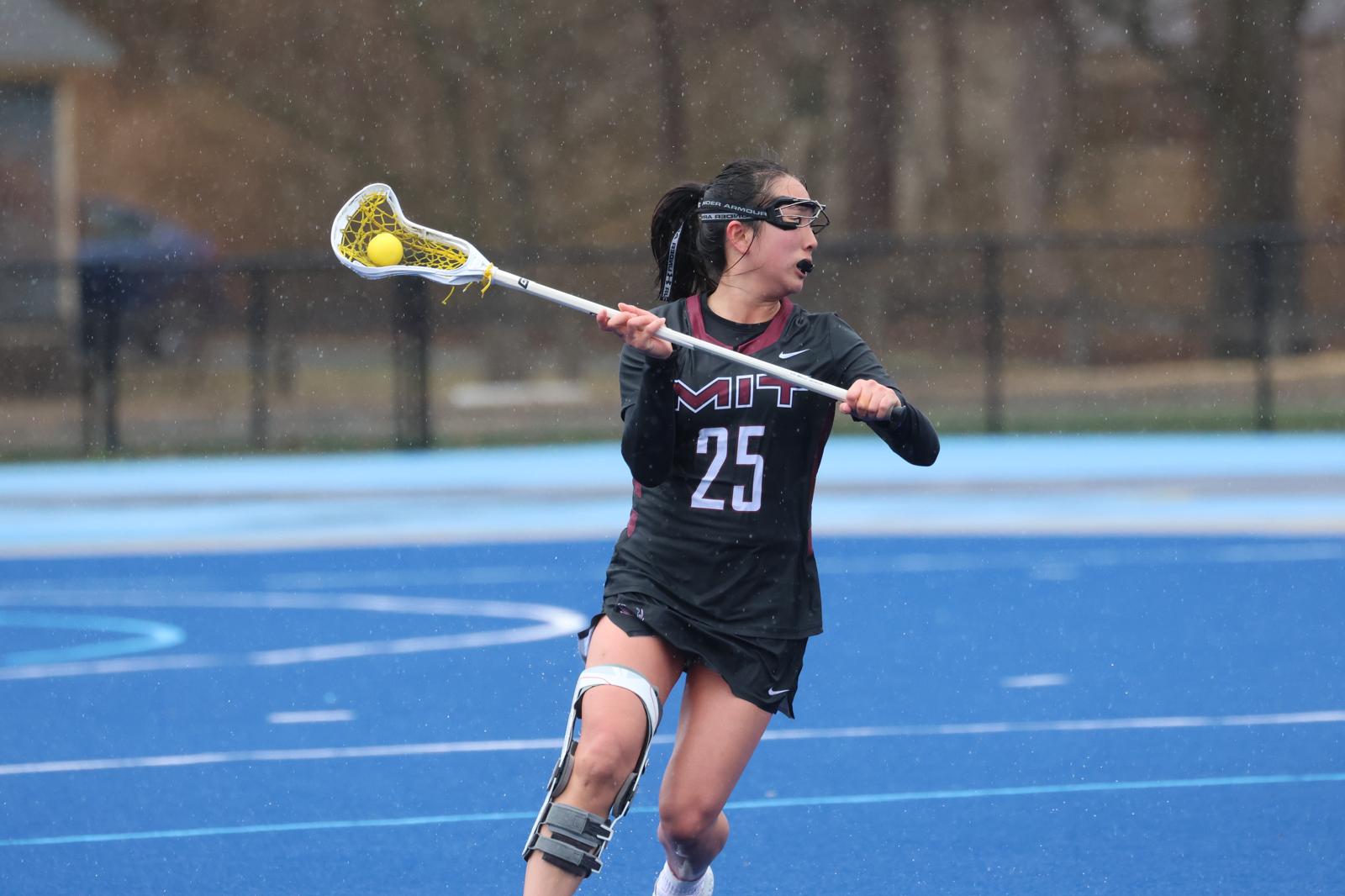 Girl playing lacrosse wearing an MIT jersey and holding the ball.