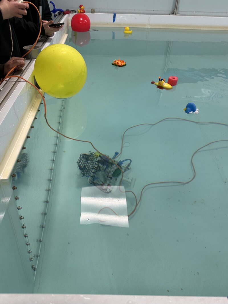 A robot made mostly of PVC pipes submerged in the pool in the previous image.