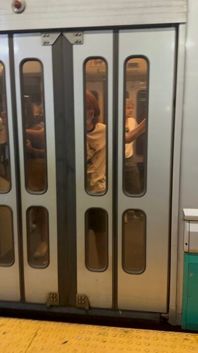 A blurry photo of the doors of a train. Behind them, a boy with red hair can be vaguely seen covering his mouth in shock and laughter