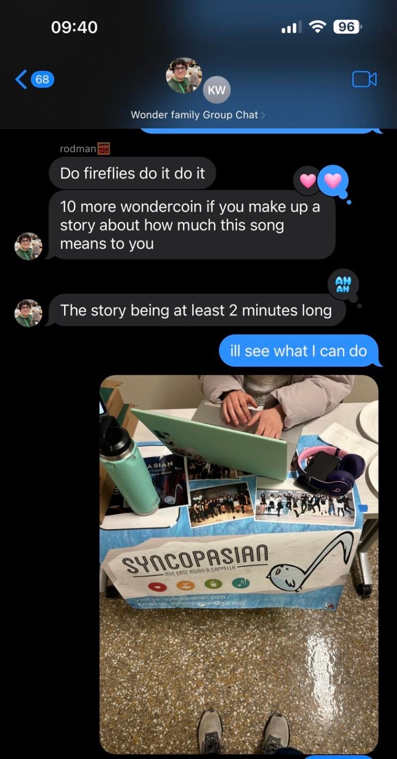 Carlos says: “Do fireflies do it do it. 10 more wondercoin if you make up a story about how much this song means to you. The story being at least 2 minutes long” I reply: “ill see what I can do.” Then I send a photo of a light-blue table, with a banner printed with “SYNCOPASIAN – MIT East Asian A Cappella” and a cartoon eighth-note fish logo. On the table sit a turquoise water bottle, an open mint-green laptop, headphones, and several small photos of the a cappella group. A pair of sneaker-clad feet poke into the bottom edge of the frame, suggesting that I’m looking down at the table.