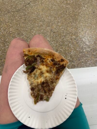 A picture of a plate of cheesesteak pizza balanced on someone's seated legs