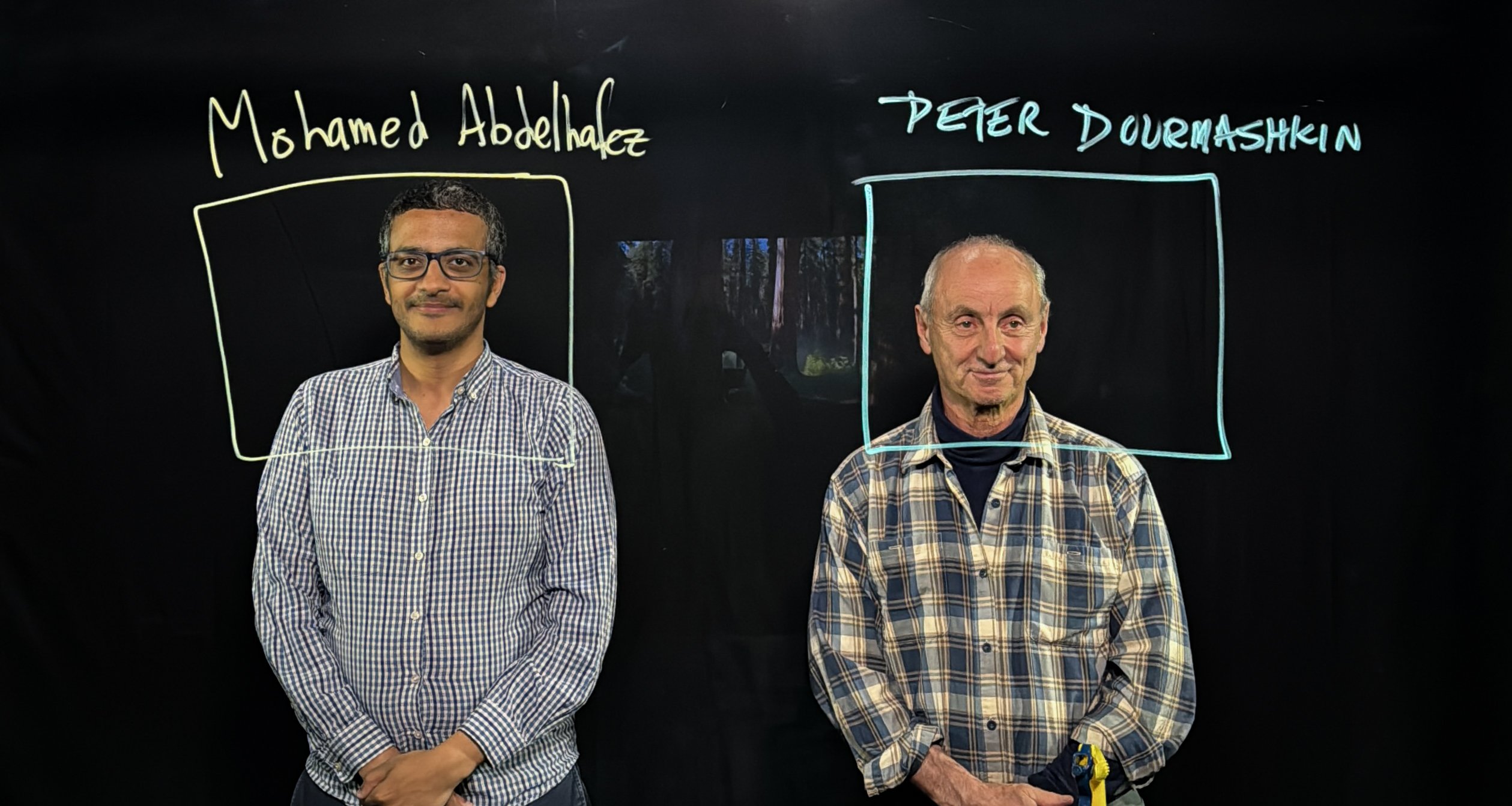 Photo of professors Mohamed Abdelhafez and Peter Dourmashkin drawing frames around themselves with their names using a transparent dry erase board