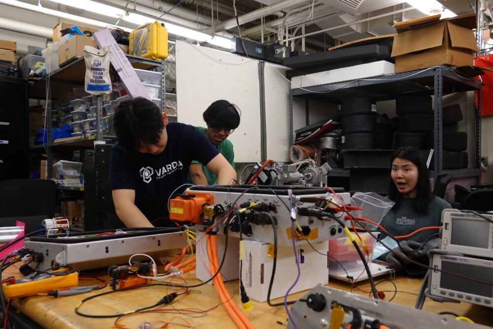 A picture of three people working on a mass of electronics on a table