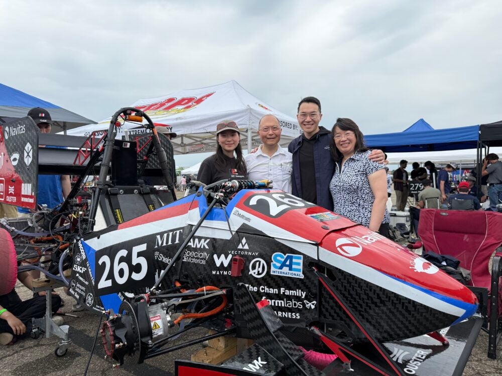 A smiling family standing behind a red and black racecar