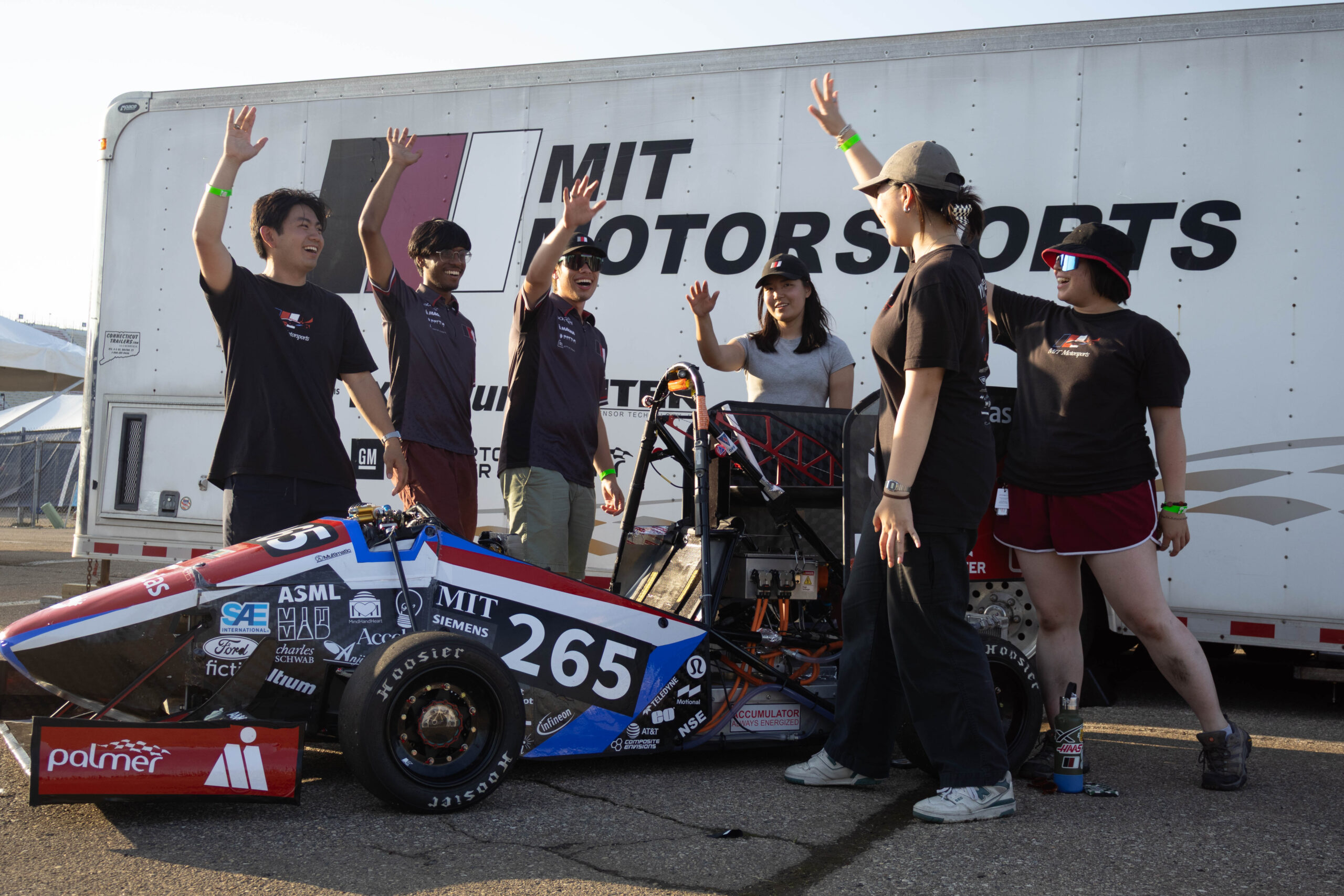 A group of people throwing their hands up, behind a red and black racecar