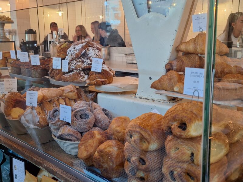 A bakery display full of pastries like croissants, pain au chocolat, and pastries dusted with sugar. Warm lighting creates a cozy, inviting ambiance.