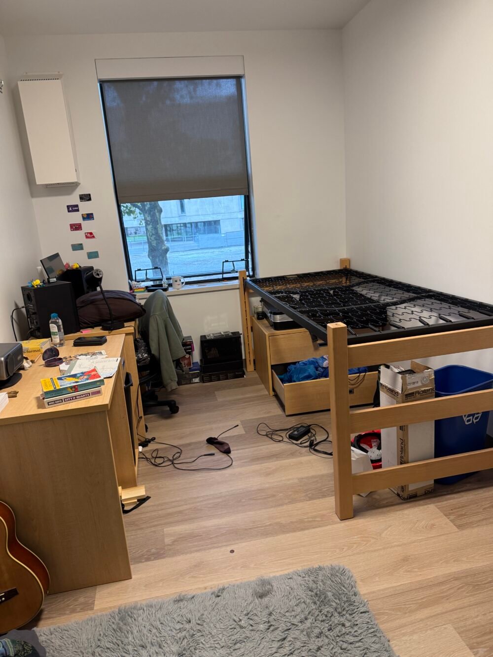 messy bedroom with 2 desks and a mattress frame without a mattress