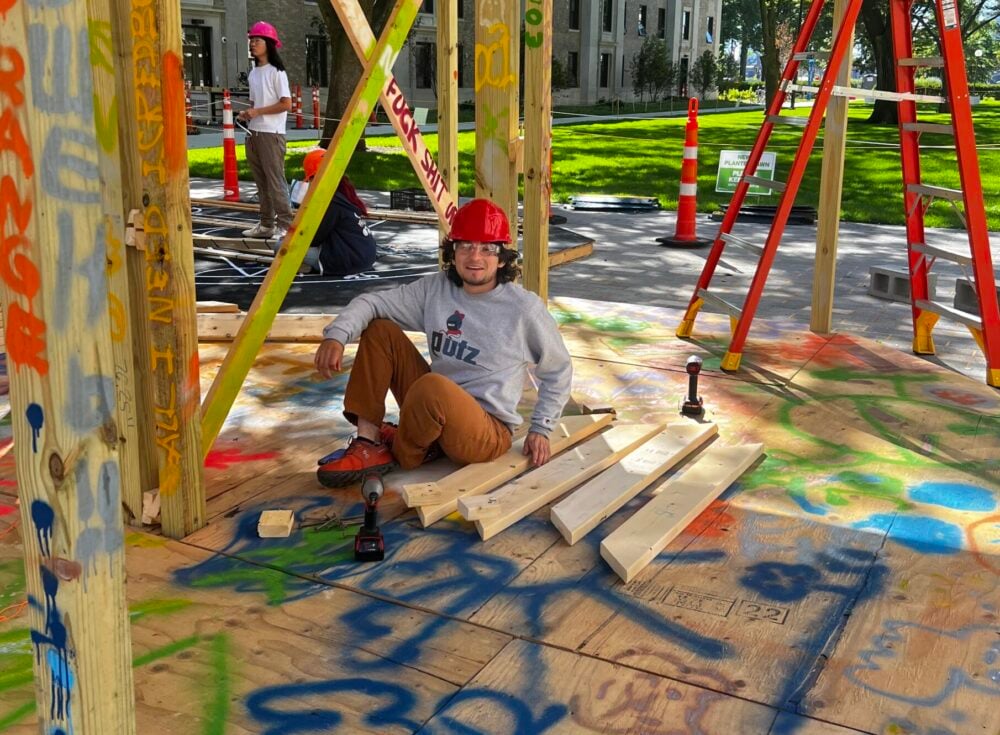person sitting in wood construction site with lots of graffiti like drawings