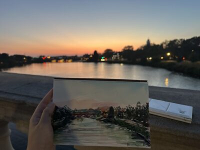small painting of a sunset over the Charles river displayed in front of said scene irl