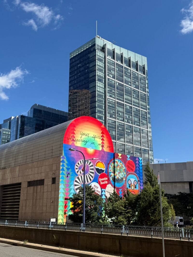 a building with a colorful mural on the front and tall modern skyscrapers in the background