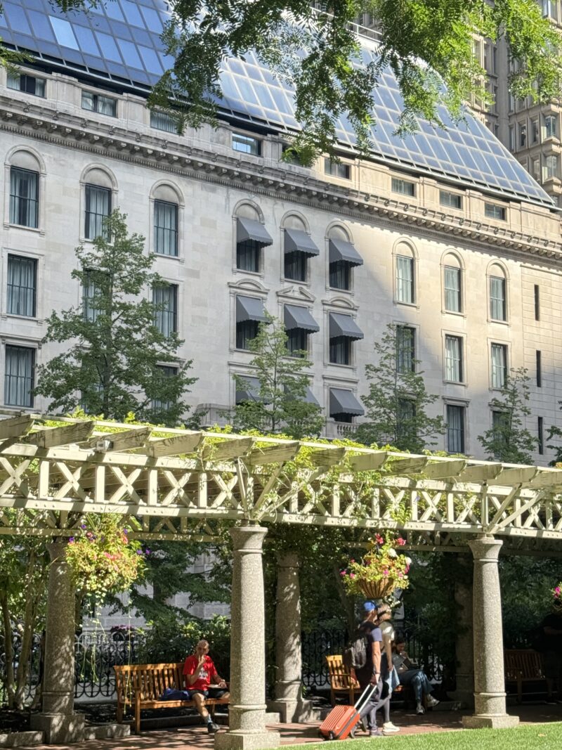 a pergola in front of a historic looking building in a park