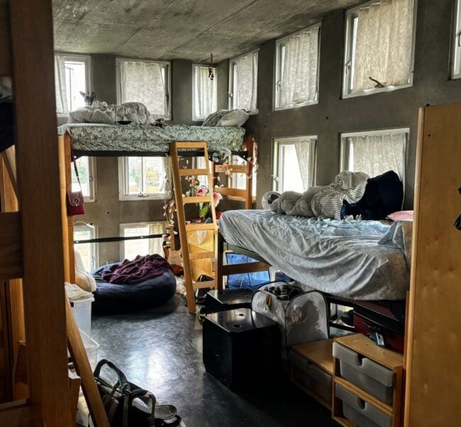 picture of room, depicting two perpendicular walls with grid of dozens of windows, and bunk beds placed against said walls