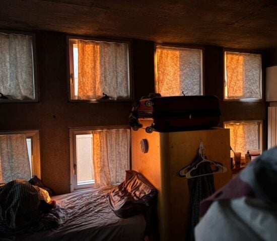 another view from inside our room at sunset from my perspective sitting on top of my bunk, showing eight windows with curtains illuminated orange