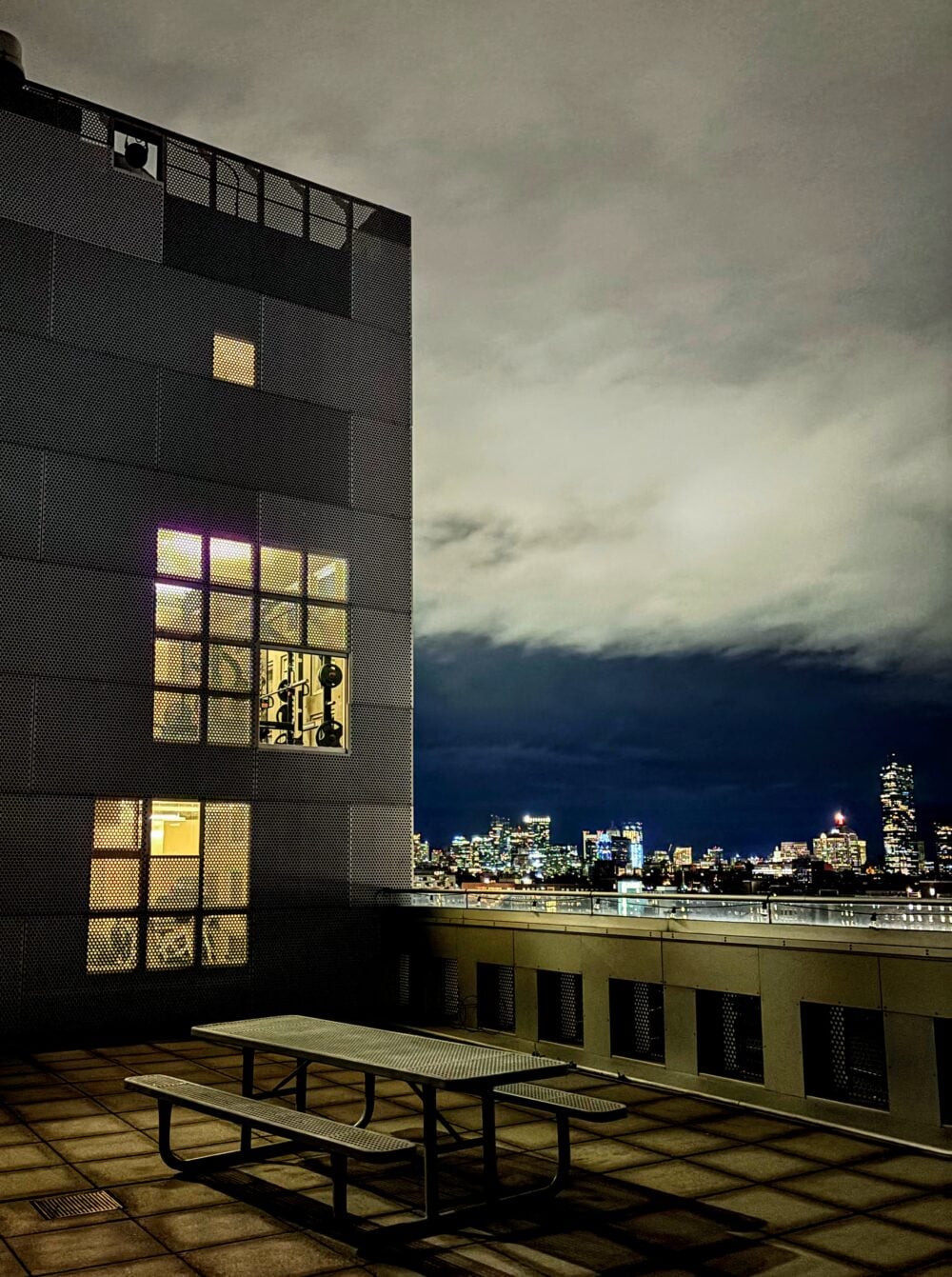 balcony with bench, with b tower on background of left side of image towering in the distance, and boston skyline on the right side