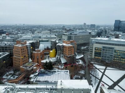 view of stata center from above with roof covered in snow; somerville and cambridge stretch in the distance beneath a bleak sky