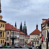 A cobblestone street lined with historic European buildings featuring red-tiled roofs and ornate details. In&hellip;