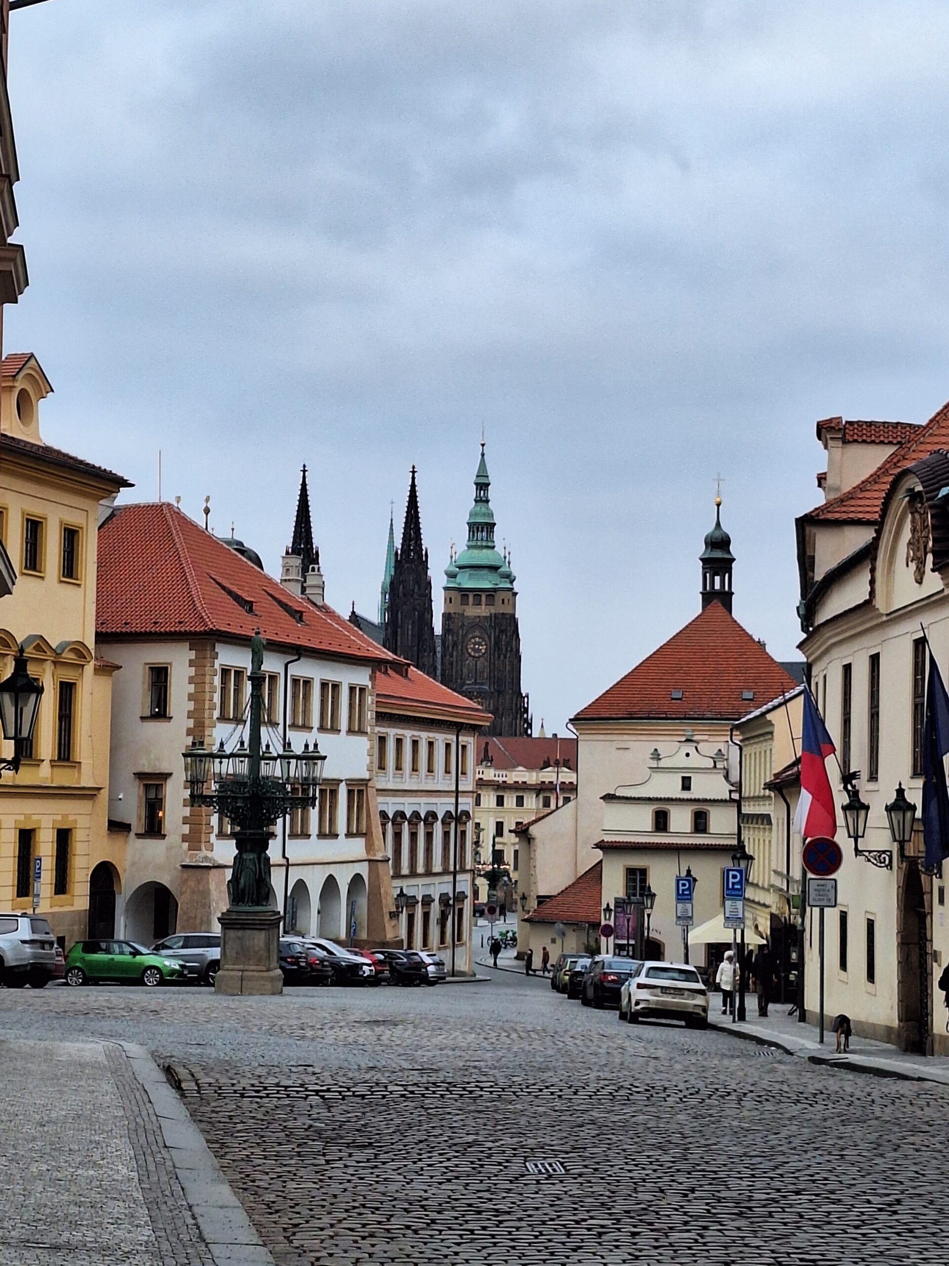 A cobblestone street lined with historic European buildings featuring red-tiled roofs and ornate details. In&hellip;