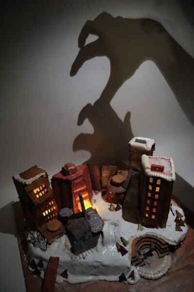 a gingerbread structure in the dark with shadow hands behind it