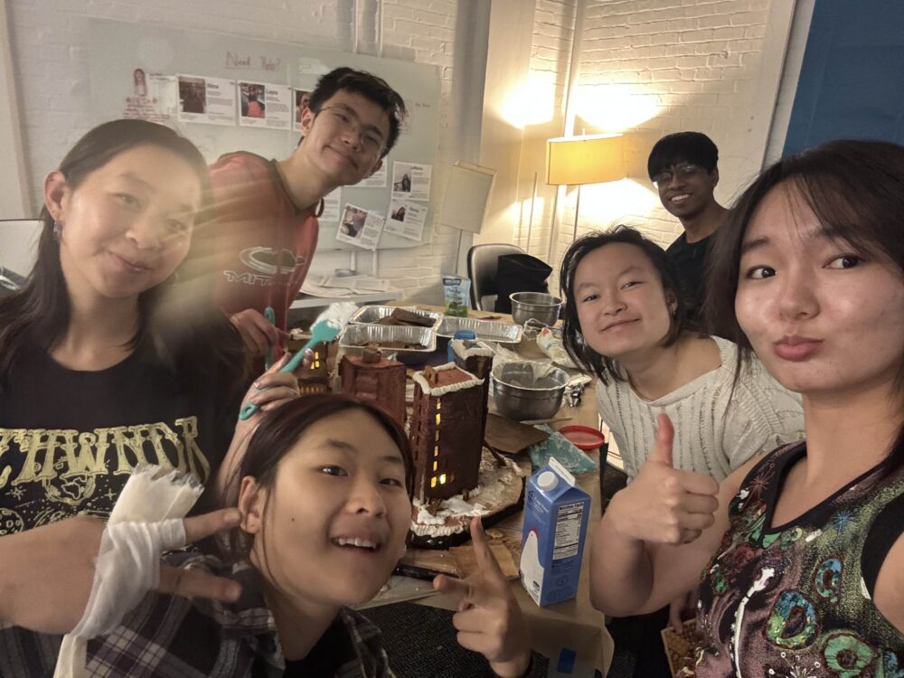 a selfie of many people posing around a gingerbread structure