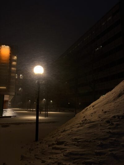 vast snow pile towering over solitary streetlight at night illuminating stray snow particles