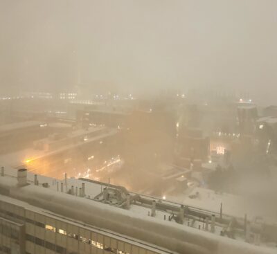 blurry snow-covered roofs as seen from above, with streetlights and windows penetrating the snowy haze