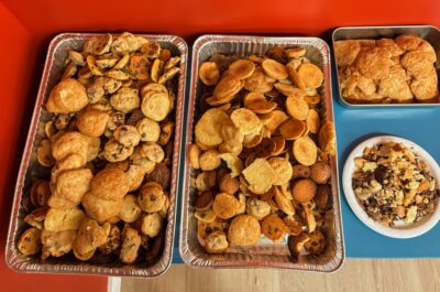 two large aluminum tins on a table filled to the brim with assorted chocolate chip and plain cookies