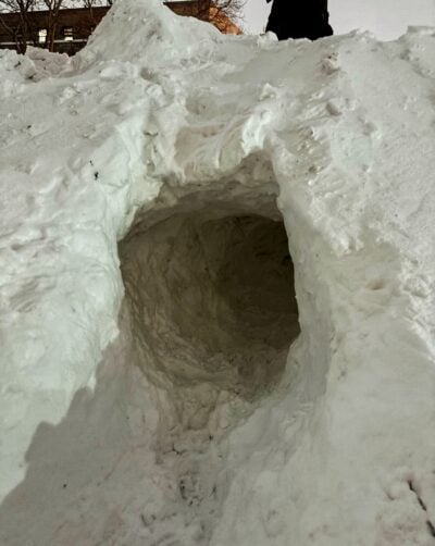 small horizontal cave entrance around one meter high in a snow pile