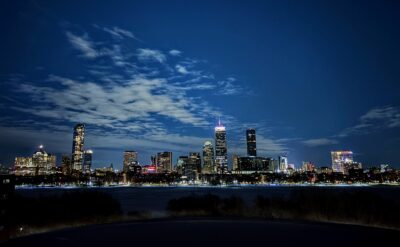 boston skyline at night seen from the upper floors of a building, with a frozen charles river in the foreground and a deep dark partially clouded sky in the background