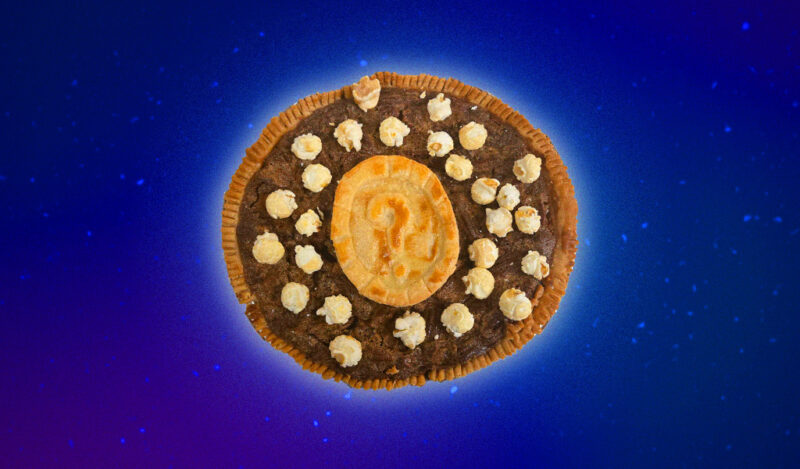 A pecan pie with a MIT Mystery Hunt coin made out of crust on top, sprinkled with kettle corn