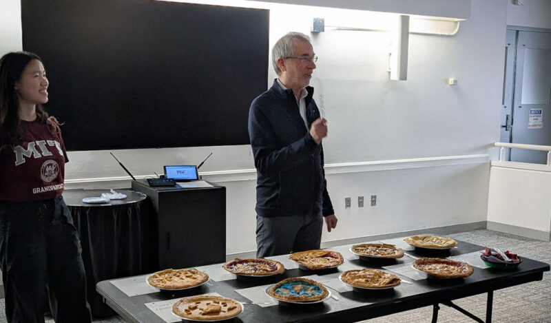 Stu stands in front of a table with 10+ pies and is the middle of talking.