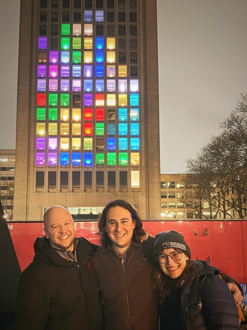a photo of the green building with colorful lights and three people standing below it 