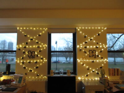 Three windows facing the charles river, with the wall space between the windows decorated with caricatures and string lights