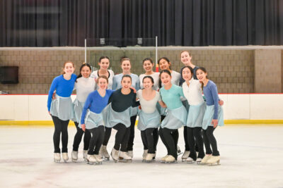 group of girls smiling and standing on the ice in two rows 