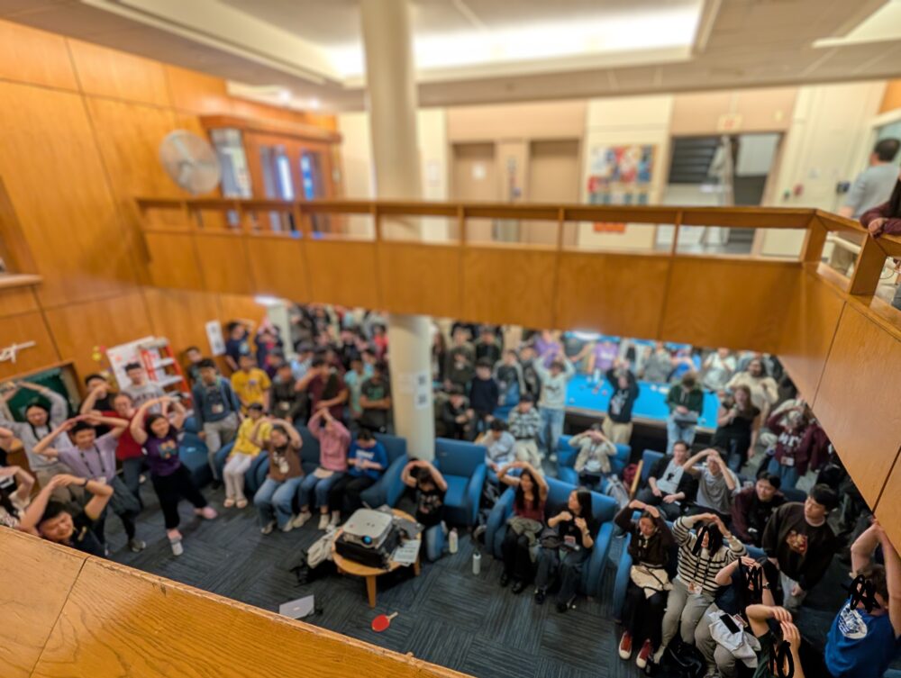 blurry picture of ~75 people in a basement room, signing the O in the chappell roan hot-to-go dance