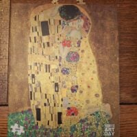 A jigsaw puzzle box showing the puzzle (Klimt’s painting “The Kiss”) laying on a brown&hellip;