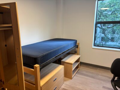 empty and new dorm room with plain bed without mattress cover above unadorned wooden cabinets