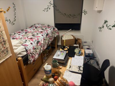 dorm room with bed positioned at a slant relative to the walls so that there's an empty corner space, with a desk at the same angle to the right of the bed