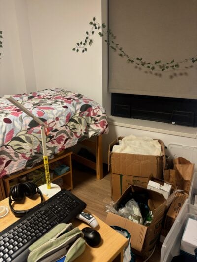 desk and bed in background next to quadrilateral-shaped floor space with storage boxes full of clothes