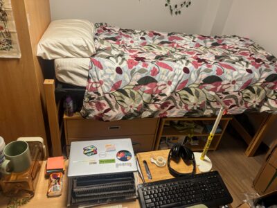 diagonal bed with cabinets underneath and laptop and keyboard on desk in foreground