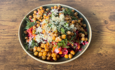 a plate of mostly chickpeas with pink slaw peeking through, covered in chopped herbs and grated cheese