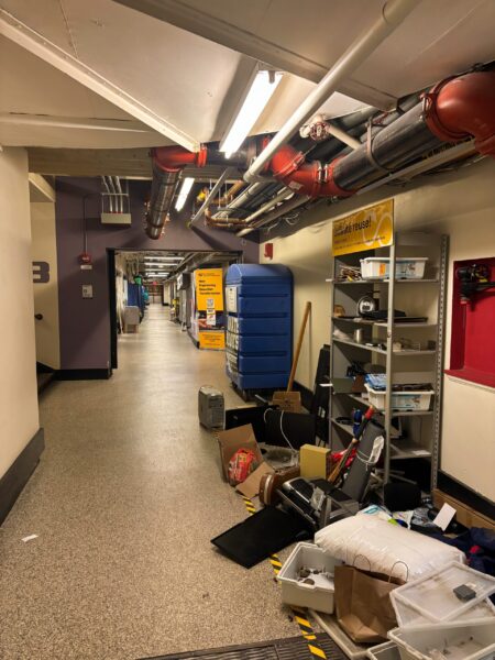 shelf along the side of a basement corridor filled with electronics and clothing