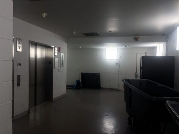 dark section of a corridor with elevator doors to the left, a vending machine to the right, and double doors in the center
