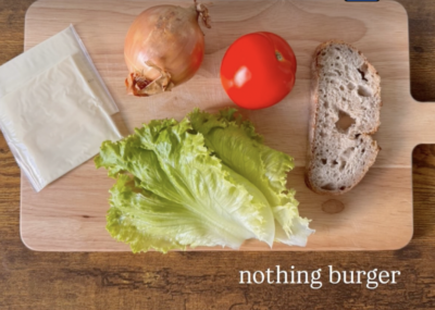 a wooden cutting board with a slice of cheese, a small onion, a tomato, two leaves of lettuce, and a slice of sourdough bread