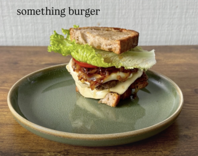 an assembled burger with the lettuce, tomato, caramelized onions, and melted cheese peeking out.