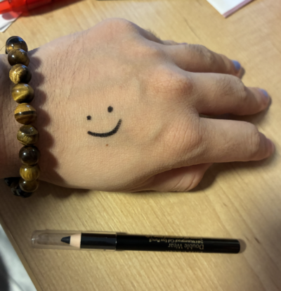 an eyeliner pencil next to a hand with a smiley face drawn on it (in eyeliner)