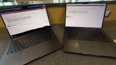 Photo of two laptops side by side on an airport counter, both displaying MIT PE registration pages.