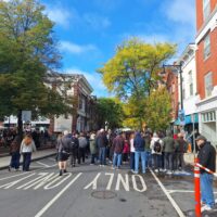 City street festival with a crowd of people, trees lining on the street, and shops&hellip;