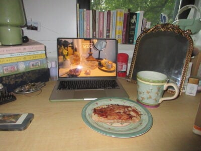 a desk, with a laptop, a mug, and a plate of raspberry toast