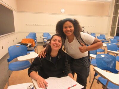 a photo of two smiling friends in an empty classroom